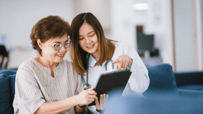 The Importance Of Hydration In North Dallas, Tx: Understanding The Serious Health Risks For Seniors 1 A Healthcare Worker In A White Lab Coat Shows An Older Woman Information On A Digital Tablet.